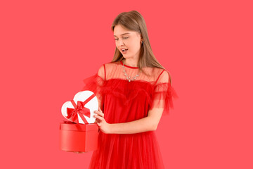 Surprised young woman with gift boxes on red background. Valentine's Day celebration