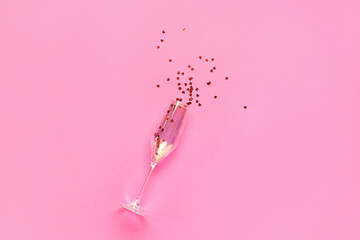 Champagne glass with heart shaped confetti on pink background. Valentine's Day celebration