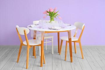 Dining table with setting and tulip flowers served for International Women's Day celebration near color wall in room