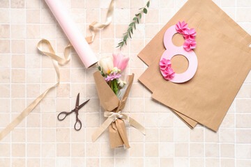 Composition with mini bouquet of beautiful spring flowers in wrapping paper, figure 8 and scissors on beige tile background. International Women's Day