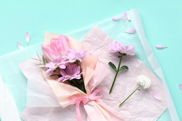 Composition with mini bouquet of beautiful spring flowers in wrapping paper on turquoise background. International Women's Day