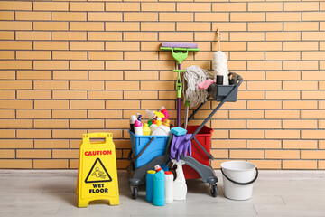 Janitor's trolley with cleaning supplies, caution sign and floor mop near brick wall