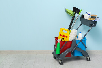 Janitor's trolley with cleaning supplies and caution sign near blue wall