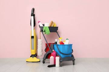 Janitor's trolley with cleaning supplies and vacuum cleaner near pink wall