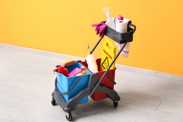 Janitor's trolley with cleaning supplies and caution sign near yellow wall