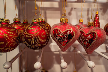 Red Christmas ornaments with gold glitter patterns hanging from a stand and spreading a festive mood.