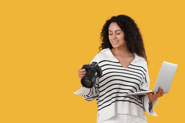 Fototapeta premium Female African-American photographer with camera and laptop on yellow background