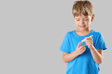 Little diabetic boy using lancet pen on grey background