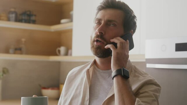 Man has phone conversation and showing disappointment while standing in a modern kitchen environment