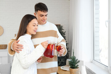 Happy couple pouring delicious mulled wine into glass at home