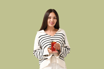 Beautiful young happy Asian woman with glass of delicious mulled wine on green background