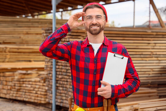 Male carpenter in safety goggles with clipboard at sawmill