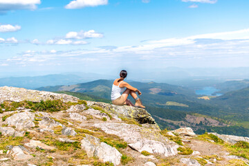 A healthy young woman sits at the summit peak of Mount Spokane State Park looking over the valleys and lakes of Spokane, Washington State and surrounding area.