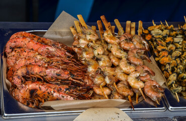 Close-up of appetizing grilled shrimp and assorted seafood skewers on display at a market stall, showcasing vibrant colors and inviting textures. 