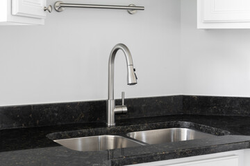 A kitchen faucet detail with white cabinets, a black granite countertop, and stainless steel sink.