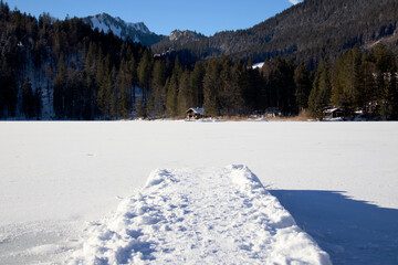 Steg mit Schnee im Winter über einen zugefrorenen See