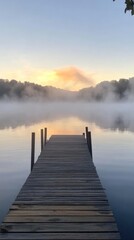 Obraz premium A serene morning scene featuring a wooden dock extending into a misty lake, with soft sunlight illuminating the horizon.