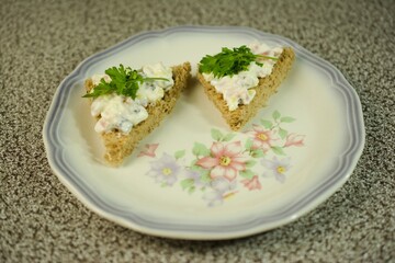 Delightful whole-grain bread triangles topped with a creamy salad mix and garnished with fresh parsley, served on a floral-patterned plate.