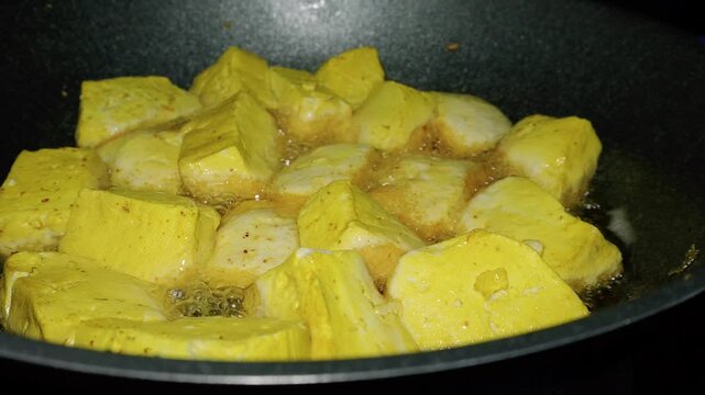 the process of cooking yellow tofu by frying it until the color turns golden brown
