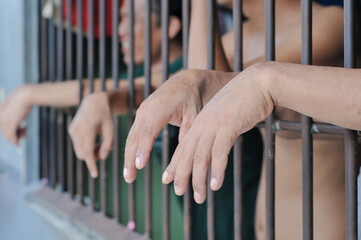 prisoner's hands behind bars with black background