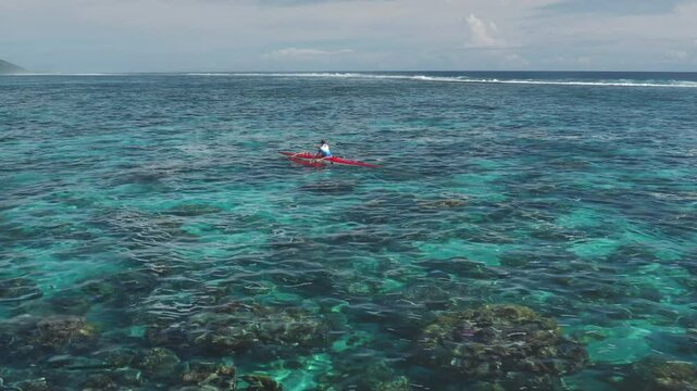 Aerial drone footage captures a sportsman kayaking in the crystal-clear turquoise waters of Tahiti. French Polynesia. Showcasing the vibrant coral reef below and the lush green island in the distance