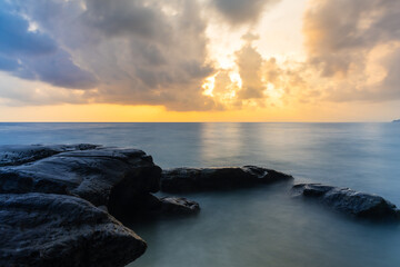 sunrise dramatic sky over sea horizon from rocky shore at dawn long exposure shot