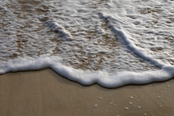 sea water white foam rolling waves with sandy beach at morning