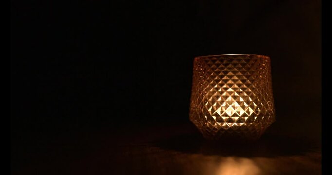 A candle flame flickers in the glasswork illuminating the darkness, and the focus shifts towards the end of the video, 4K, 60 fps