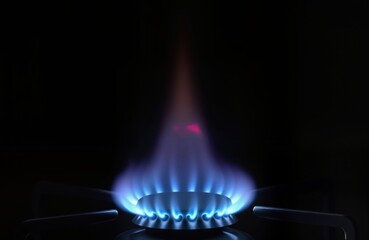 Gas burner ignites with blue flames. Hot energy source in dark kitchen. Cooking process in progress. Image shows stove burner. Gas fuel creates heat. Household kitchen appliance in action. Modern