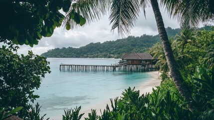 Overwater bungalow on tropical beach seen through palm trees.