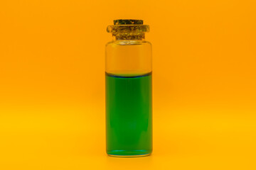 Corked glass bottle with green liquid on yellow background