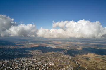 Aerial view from airplane window at high altitude of distant city covered with white puffy cumulus clouds