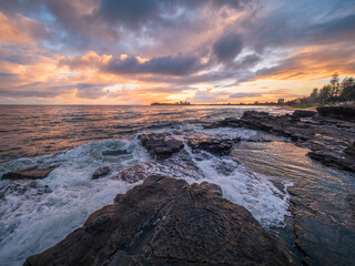 Obraz premium Colourful Coastal Sunrise with Waves on Rocks