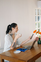 Freelancer woman working remotely in cafe, with laptop, coffee, and cellphone. Casual outfit,...