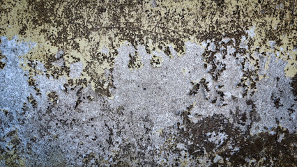 A close-up view of a weathered wall with peeling paint revealing layers of yellow and gray hues, creating an abstract and textured surface