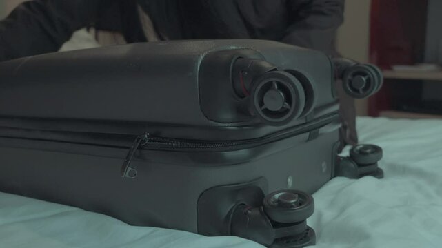 A woman is sitting on a bed and opening her suitcase. The scene is dark and moody, with a sense of mystery and anticipation. The woman is in the process of packing or unpacking her belongings