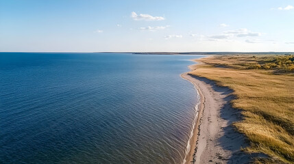 Aerial view of serene coastline, sandy beach, grassy dunes, clear sky, coastal travel.