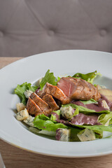 Baked piece of meat among green salad and vegetables on table in restaurant