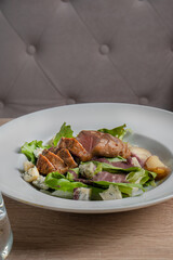 Baked piece of meat among green salad and vegetables on table in restaurant