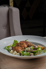 Baked piece of meat among green salad and vegetables on table in restaurant