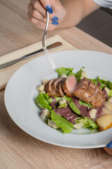Baked piece of meat among green salad and vegetables on table in restaurant
