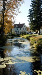Obraz premium A serene scene featuring a house by a calm stream surrounded by autumn foliage.
