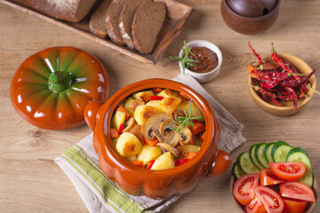 Baked potatoes with mushrooms in ceramic bowl on dining table among vegetables