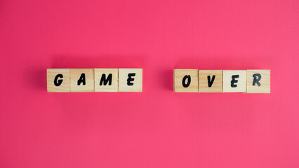The phrase GAME OVER spelled with wooden letter blocks on a vibrant pink background.