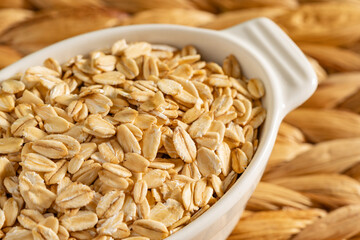 Rolled oats in a white ceramic bowl on a woven rustic surface. Ideal for breakfast, healthy snacks, or natural recipes.