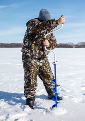 Naklejka premium A man in camouflage clothing is standing in the snow with a blue ice auger