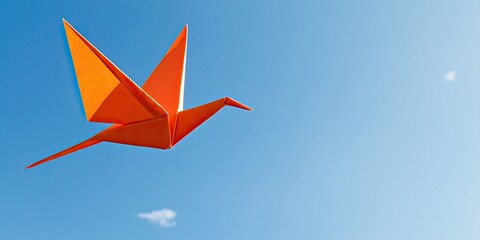 An orange origami crane soars against a clear blue sky, symbolizing peace and creativity.