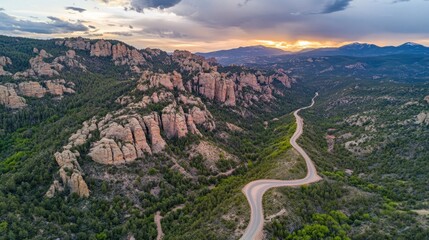 Aerial view of winding mountain road at sunset, showcasing dramatic rock formations and lush green valleys.