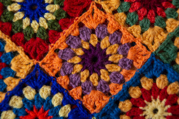 A square crocheted from wool yarn in burgundy, yellow, lilac and orange colors.