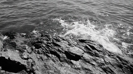 Black and white photo of ocean waves crashing on dark rocks.